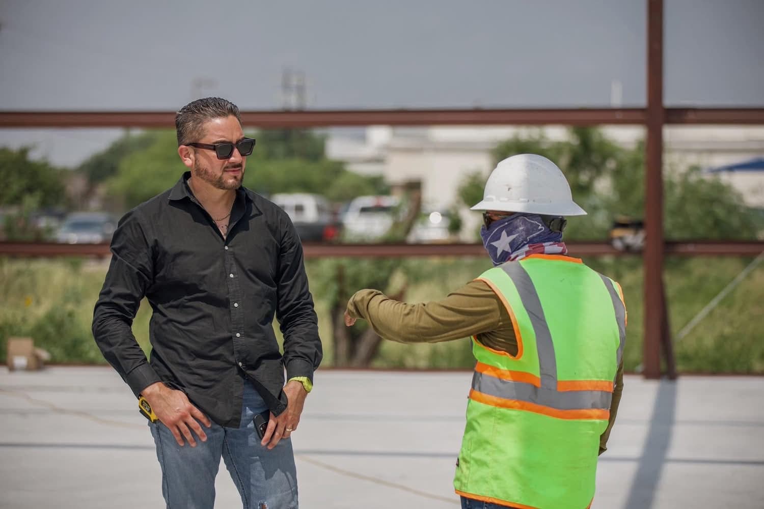 Efrain Gomez Jr. talking with a crew member wearing a hard hat and safety vest on an outdoor job site